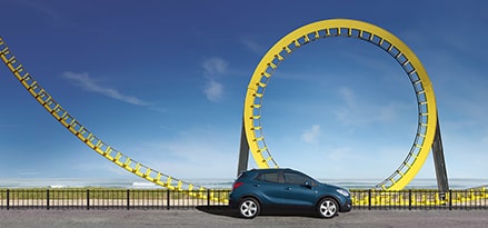 Ein dunkelblaues Auto vor einer Achterbahn am Strand